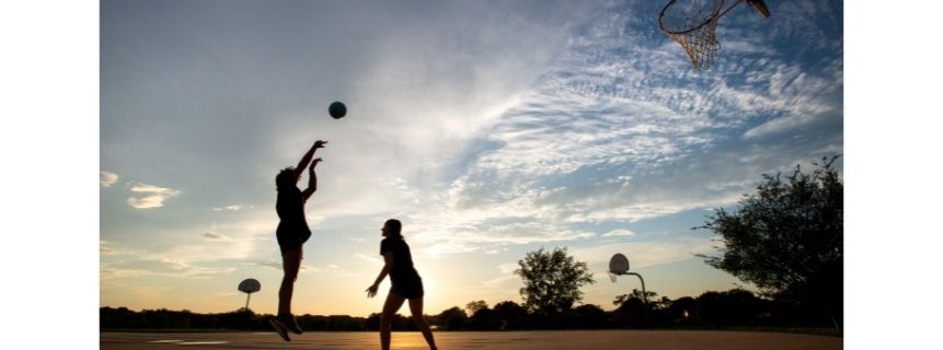 Two people playing basketball at sunset