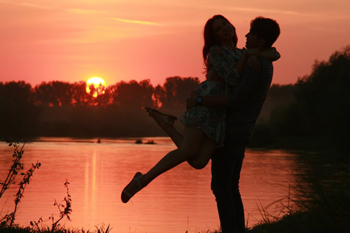 man swinging woman up into an embrace at sunset