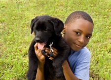 Boy holding a black puppy, both sitting in grass