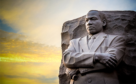 Large stone statue of Martin Luther King Jr. against blue and yellow sky