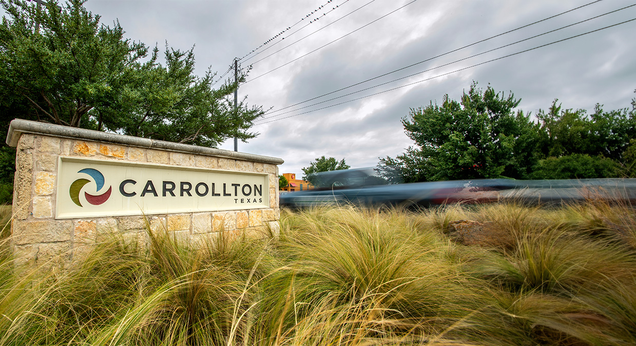 City of Carrollton stone sign with trees behind it and a truck driving past