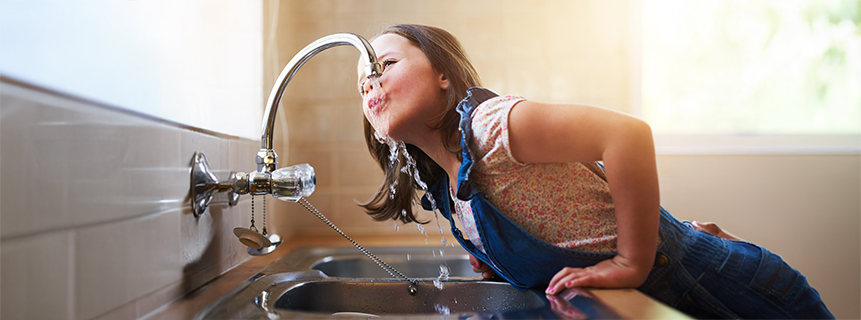 Happy young girl drinks from a water faucet in a kitchen